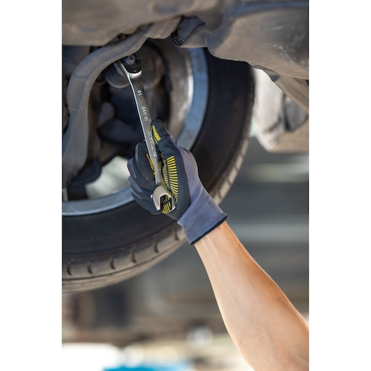 STANLEY FMMT13087-0 wrench in use near a vehicle wheel, worker wearing textured grip gloves.