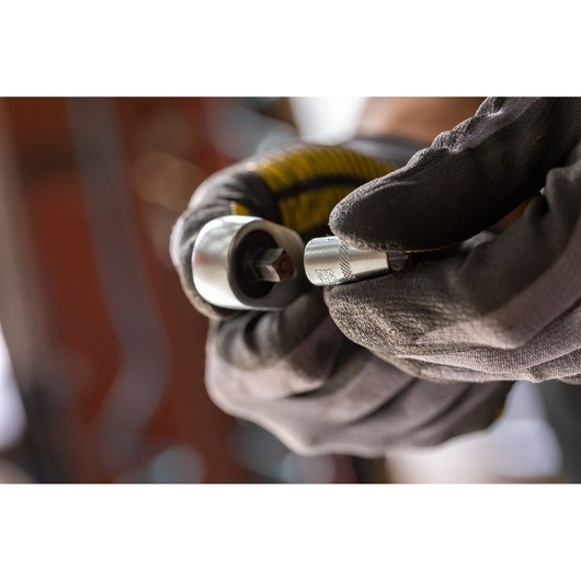 Photo of STANLEY FMMT17187-0 socket adapter held by gloved hands, close-up view.