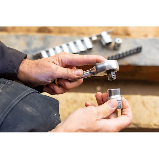 Photo of STANLEY FMMT82679-0 ratchet wrench and socket held in hands, with sockets set in background.