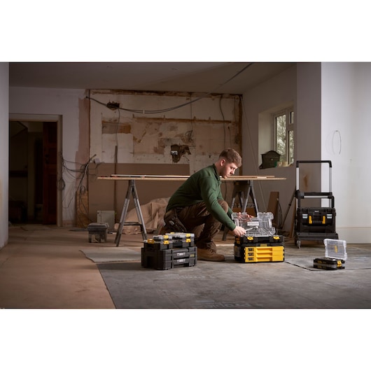 Person sorting tools with STANLEY organizer boxes in a workspace under renovation.