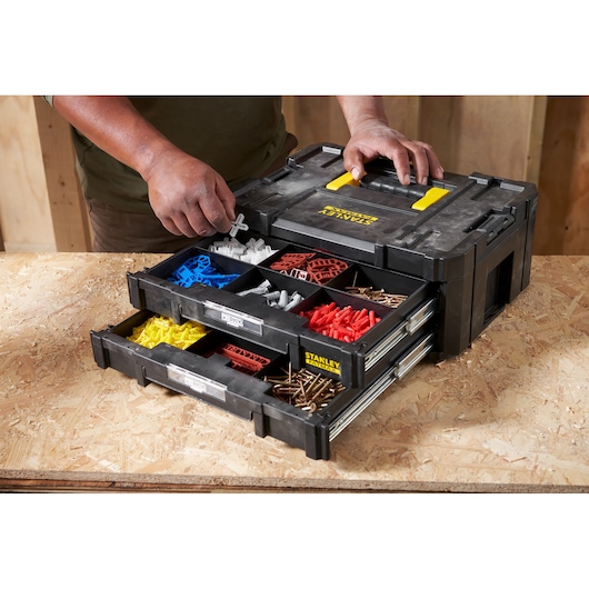 Photo of STANLEY FMST1-71969 organizer box with open drawers holding assorted screws and wall plugs on a workbench.