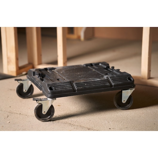 STANLEY FMST1-71972 black plastic rolling dolly with four swivel casters, shown on a workshop floor.