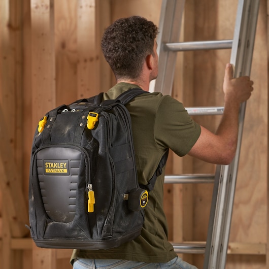 Photo of STANLEY FMST1-80144 tool backpack with yellow accents, worn by a person in a workshop, climbing a ladder.
