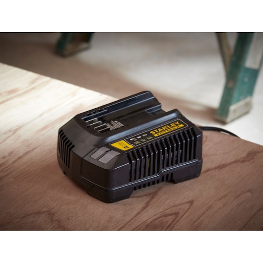 Photo of STANLEY SFMCB14 black battery charger on wooden surface, labeled FATMAX, shown in workshop setting.