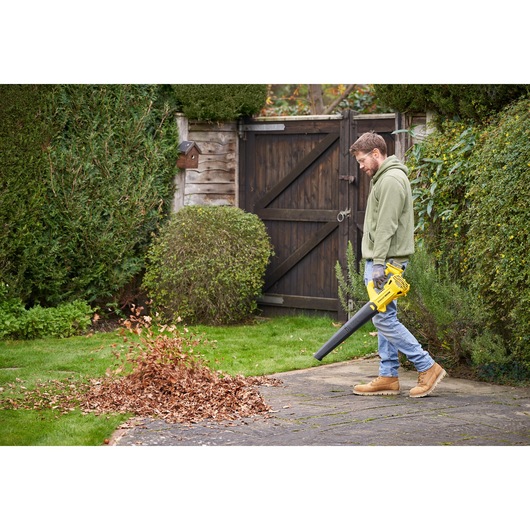 Photo of person using STANLEY SFMCBL714M1 cordless leaf blower to clear leaves from garden patio.