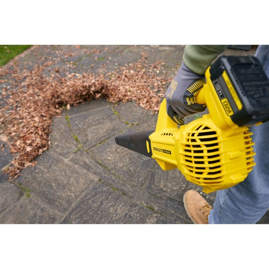 STANLEY SFMCBL714M1 leaf blower in use on outdoor stone patio, moving a pile of dry leaves.