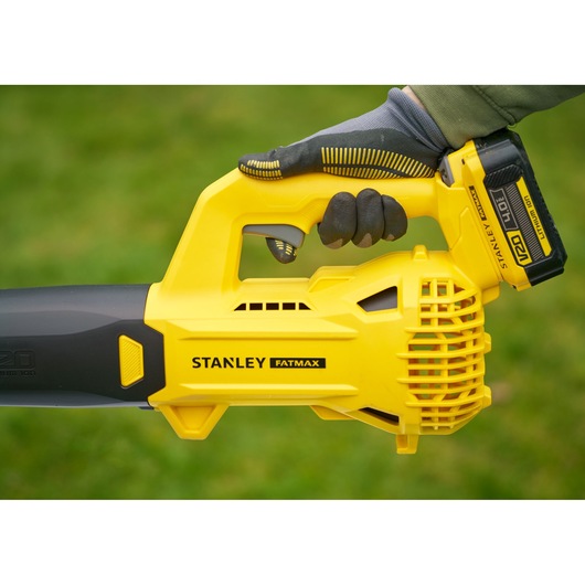 STANLEY SFMCBL714M1 yellow cordless leaf blower held in hand, side view, on grass background.