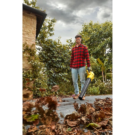 Photo of STANLEY SFMCBL7B leaf blower in use outdoors, blowing dry leaves on a patio.