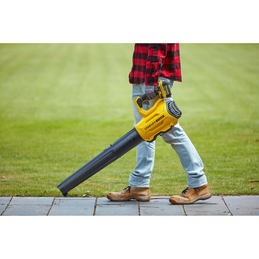 Stanley SFMCBL7B leaf blower held by person outdoors on grass wearing jeans and boots.