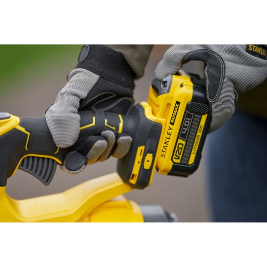 Photo of STANLEY SFMCBL7M1 cordless tool with 18V 4.0Ah battery, close-up of gloved hands operating device.