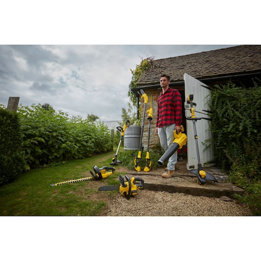 Photo of STANLEY SFMCCS630B garden power tools set displayed outside with person, various yellow tools shown.