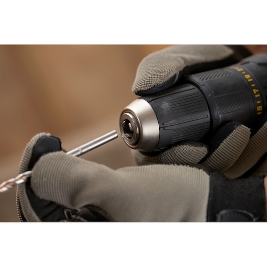 Photo of STANLEY SFMCD711B drill being fitted with a bit, gloved hands holding tool, close-up view.