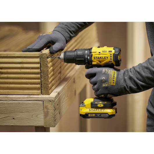 Stanley cordless drill in use, drilling into wood by a person wearing gloves and a grey long-sleeved shirt.