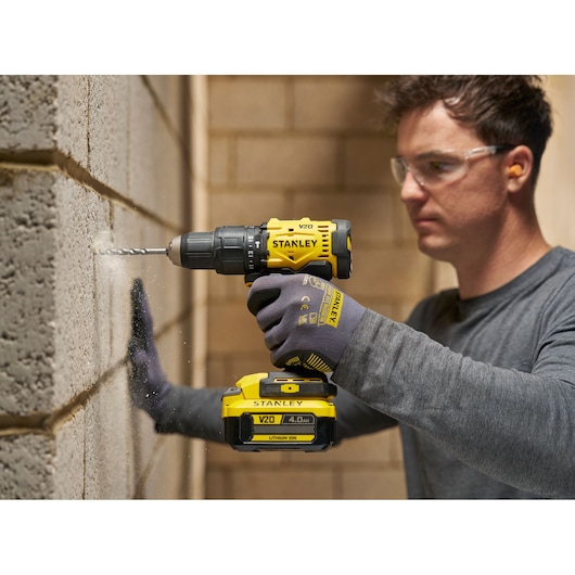 Person drills into a wall using a STANLEY V20 cordless power drill in a construction setting.