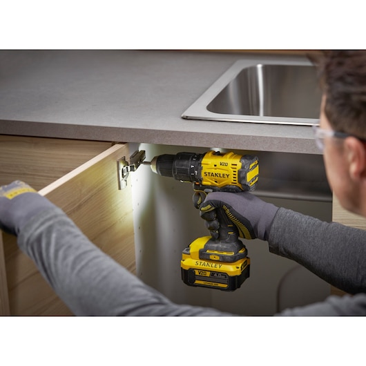 Person using a Stanley drill to install a kitchen cabinet hinge under a countertop near a sink.