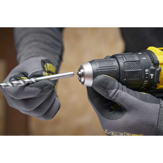 Gloved hands insert a drill bit into a yellow and black cordless drill.