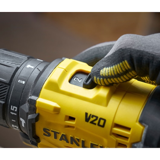 Close-up of a gloved hand adjusting speed on a yellow STANLEY V20 power drill.