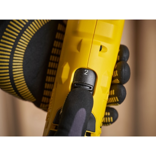 STANLEY SFMCD750D2K drill speed selector close-up, yellow body, gloved hand pressing switch.