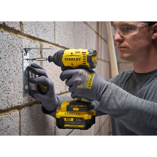 Stanley V20 cordless impact driver used to fix metal bracket to a brick wall, person wearing gloves and safety glasses.