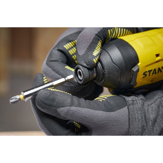 Gloved hands insert a screwdriver bit into a yellow STANLEY power tool, close-up view of the tool and attachment.