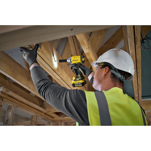 Worker uses Stanley power tool to drill into wooden beams at construction site, wearing safety gear.