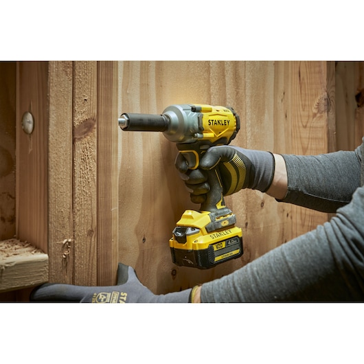 Stanley cordless impact wrench in use on wooden boards, worn by a gloved hand.