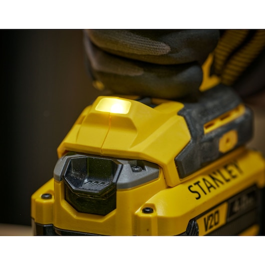 Close-up of a Stanley V20 tool with LED light on, showing detail of yellow and black casing and gloved hand.