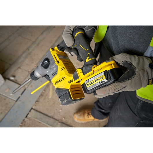 Stanley V20 cordless rotary hammer drill held by a person with gloves, on a construction site.