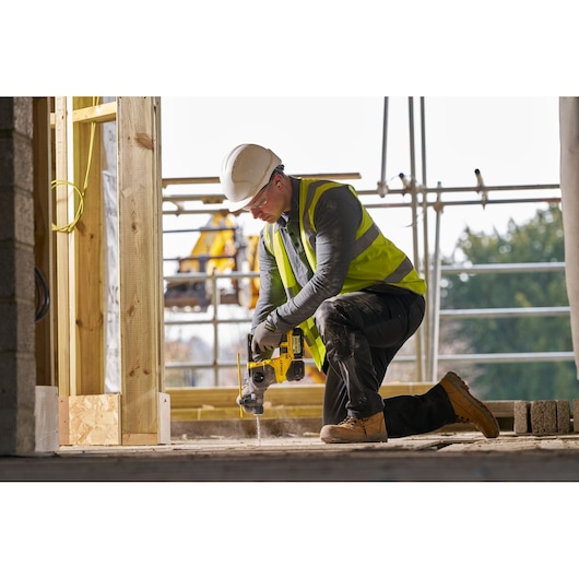 Worker in safety gear uses a yellow Stanley drill on concrete at a construction site.