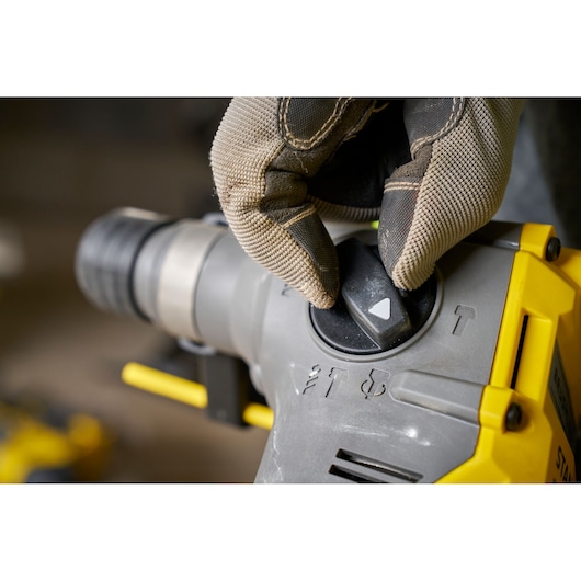 STANLEY SFMCH910R1T rotary hammer drill mode selector being adjusted with gloved hand, close-up photo.