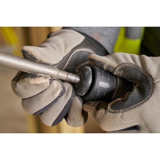Photo of STANLEY SFMCH910R1T rotary hammer drill bit change, close-up with gloves, side angle.