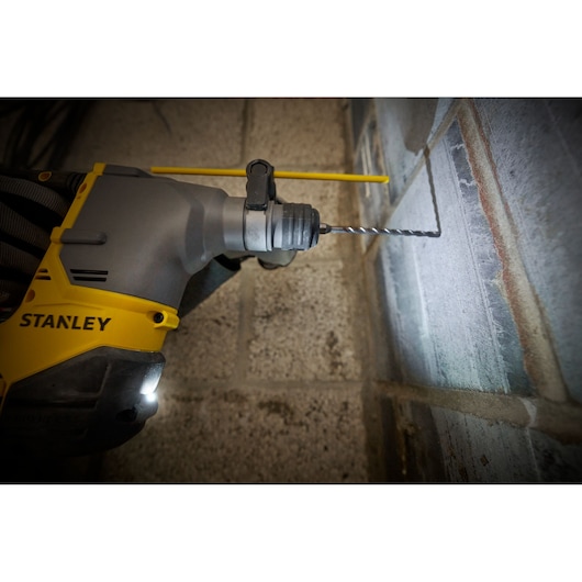 STANLEY SFMCH910R1T rotary hammer drilling into concrete wall, close-up angle, yellow and gray tool.
