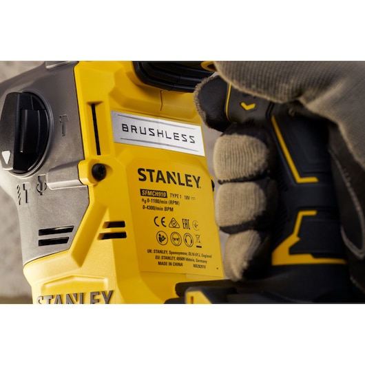 Stanley SFMCH910R1T brushless rotary hammer close-up, yellow and black body, gloved hand holding handle.