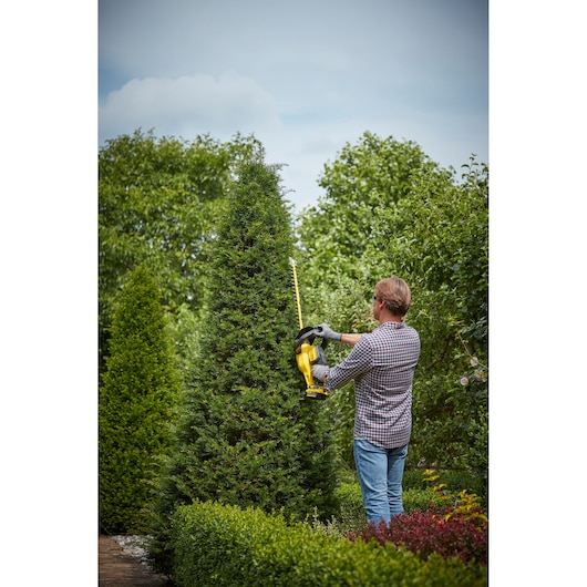 STANLEY SFMCHT855B hedge trimmer being used outdoors by a person trimming a tall green bush.