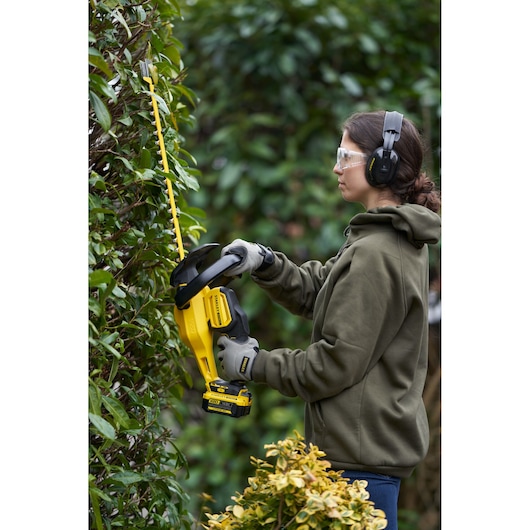 STANLEY SFMCHT855B hedge trimmer in use outdoors, yellow and black, battery-powered, garden scene.