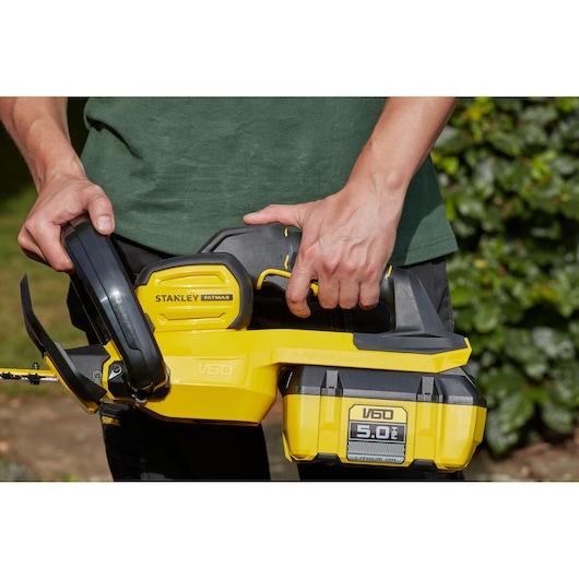 Photo of STANLEY SFMCHTB866B hedge trimmer, yellow and black, held by person outdoors.