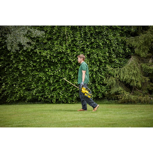 STANLEY SFMCHTB866B hedge trimmer held by person walking outdoors, green garden background.