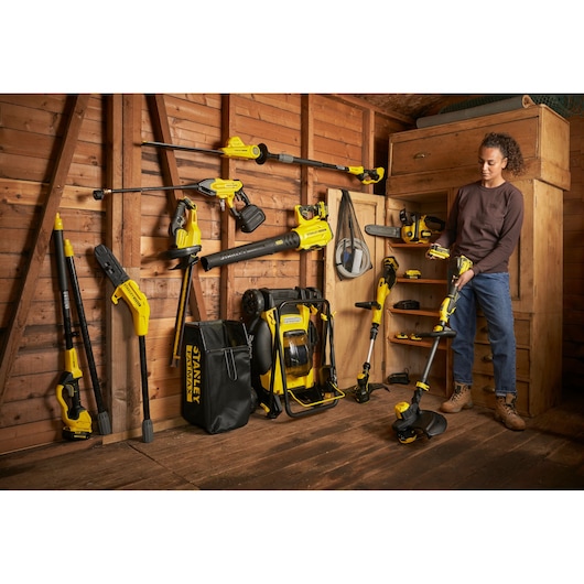 STANLEY SFMCMW2651M garden tools set in wooden shed, multiple tools displayed, person holding string trimmer.