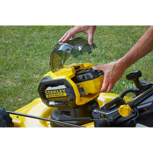 Photo of STANLEY SFMCMW2653B battery compartment being opened on yellow lawn mower.