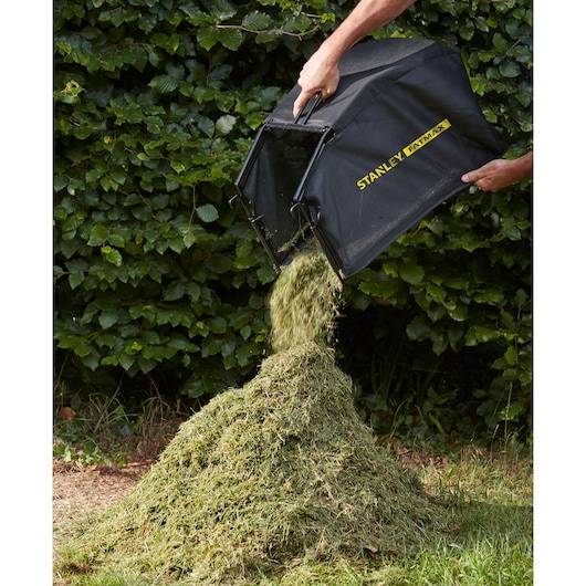 STANLEY SFMCMW2653B lawn mower grass bag being emptied, releasing grass clippings onto a pile outdoors.