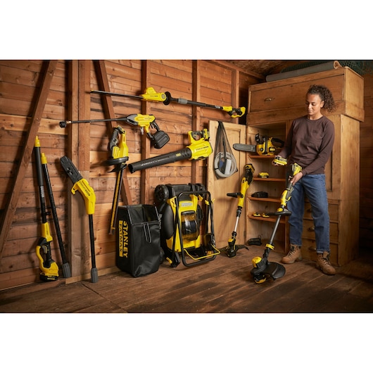 Photo of STANLEY SFMCPH845B garden power tools set arranged in wooden shed, person holding string trimmer.