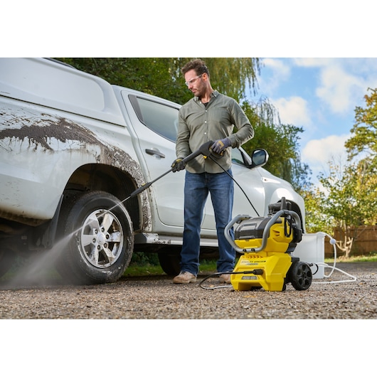 STANLEY SFMCPW1500B pressure washer used outdoors to clean muddy truck, with hose connected and water spraying.