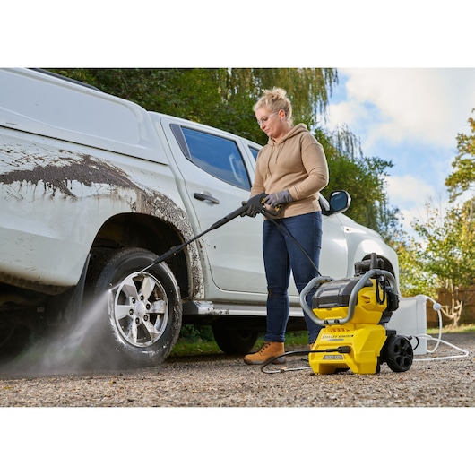 STANLEY SFMCPW1500B pressure washer cleaning a dirty white vehicle's wheel outdoors.