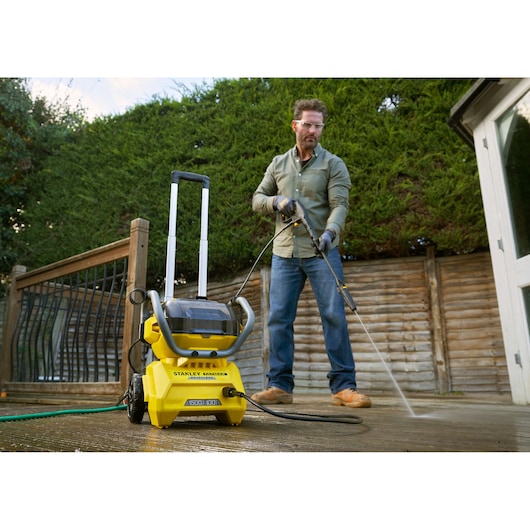 STANLEY SFMCPW1500B pressure washer on patio, shown in use by person cleaning wooden deck outdoors.