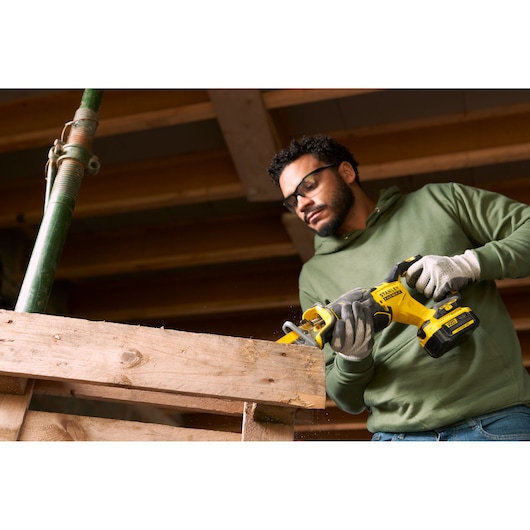 Photo of a person using a STANLEY SFMCS310B cordless reciprocating saw to cut a wooden beam on a construction site.