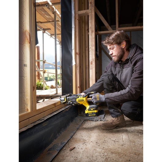 Photo of a worker using a STANLEY SFMCS311M1T cordless reciprocating saw cutting wood at a construction site.