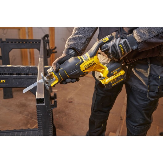 Photo of STANLEY SFMCS311M1T cordless reciprocating saw cutting metal pipe, yellow and black tool in use.