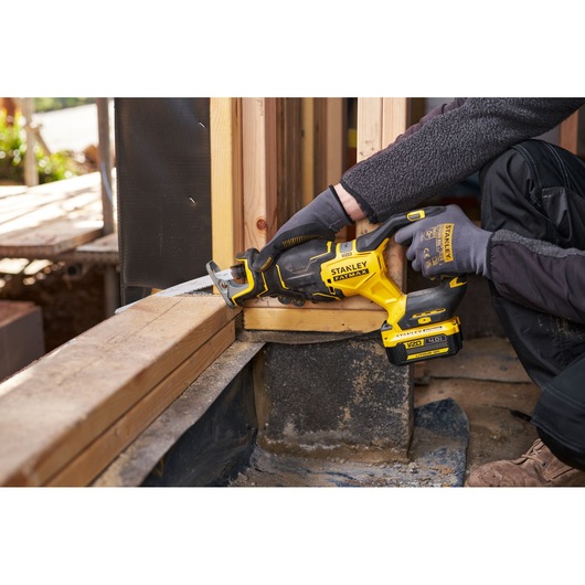 Photo of a worker using a STANLEY FATMAX SFMCS311M1T cordless reciprocating saw cutting wood at a construction site.