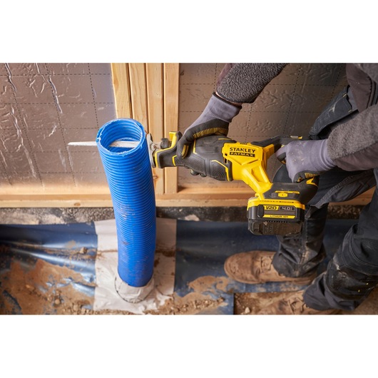 STANLEY SFMCS311M1T reciprocating saw cutting blue corrugated pipe at construction site, side angle.