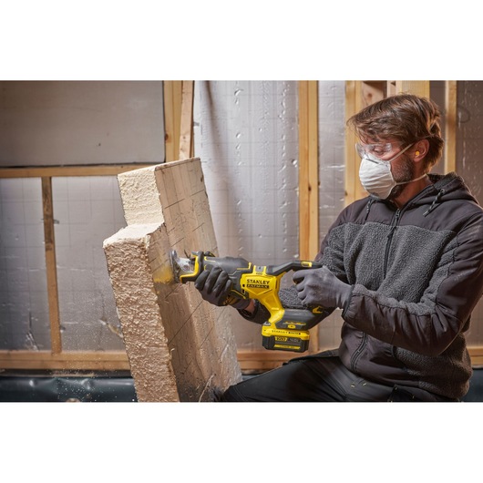 Person using STANLEY SFMCS311M1T reciprocating saw to cut foam insulation panel in construction setting.